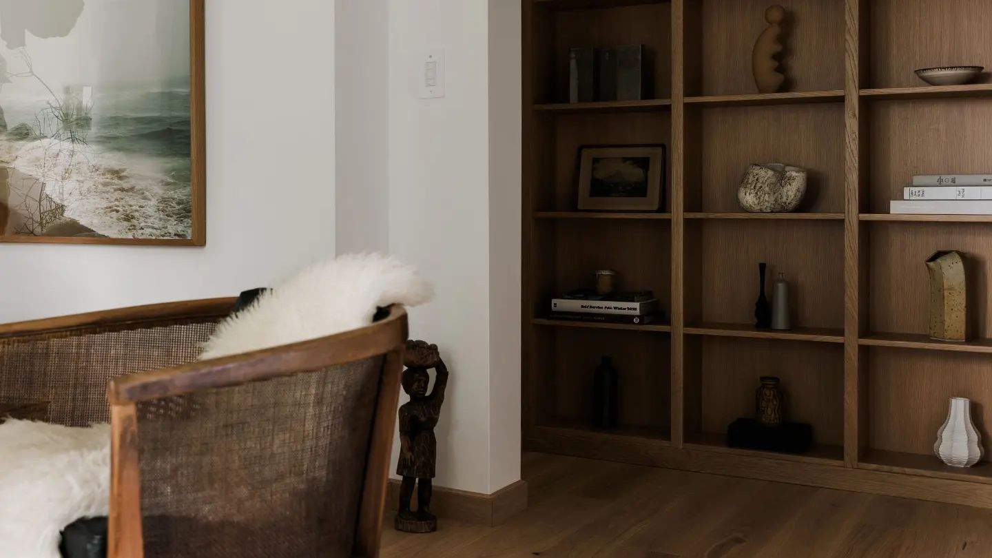 Floor-to-ceiling white oak built-in bookcase in a living room beside a cane armchair
