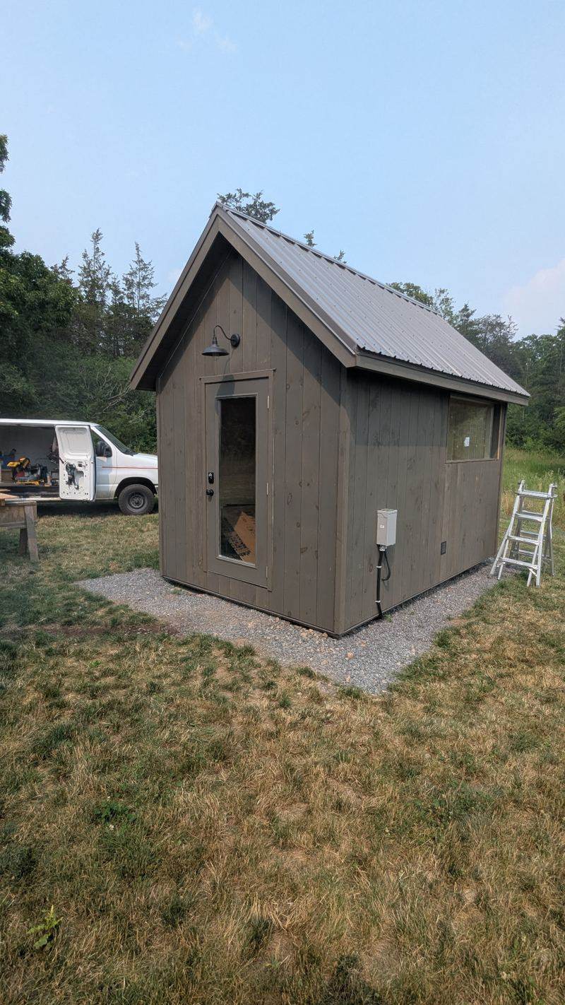 Small grey-sided outbuilding with a metal roof on a gravel pad